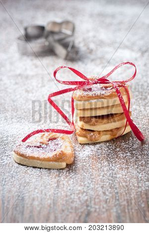 Fresh cookies with icing sugar filled with jam an cookie cutter in the background.