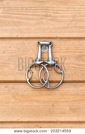 Steel horse snaffle-bit hanging on wooden background. Outdoors close-up.