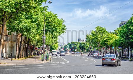 Paris, France - June 5, 2017: Avenue de l'Observatoire flanked by tall green trees from both sides. Monument of Francis Garnier is seen in the background