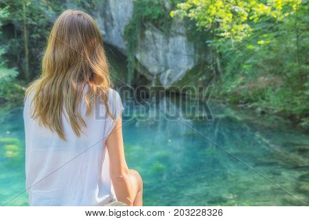Young woman sitting near the beautiful lake in nature.
