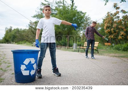 A full-length portrait of a little serious boy and a slovenly young man on a blurred natural background. A child showing thumb down to a guy throwing a bottle in the middle of the road. Copy space.