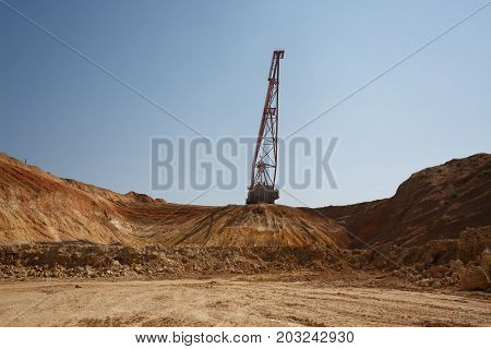 An industrial moving machine in the foundation pit. Yellow mobile crane working in the sandy quarry. Industry equipment on a blue sky background. Technology, cargo, commerce, transport concept.