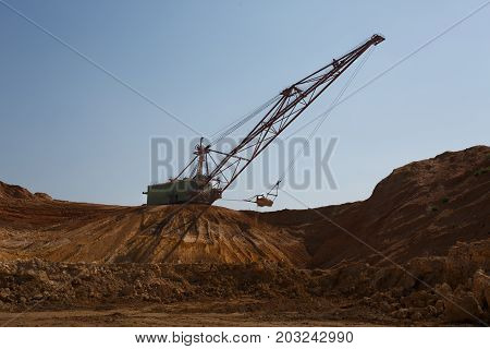 Yellow mobile crane working in the sandy quarry. An industrial moving machine in the foundation pit. Industry equipment on a blue sky background. Technology, cargo, commerce, transport concept.