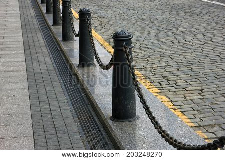 fencing of sidewalk in form of black cast iron posts with iron chains
