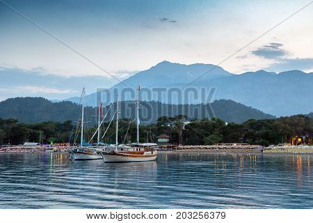 Yachts near the shore of the resort city in the evening against the backdrop of the silhouette of the mountains