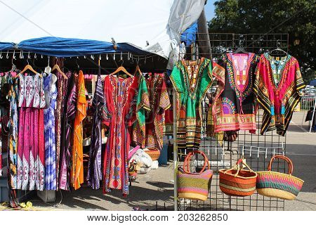 Colorful African dashikis, dresses and woven bags at an outdoor flea market
