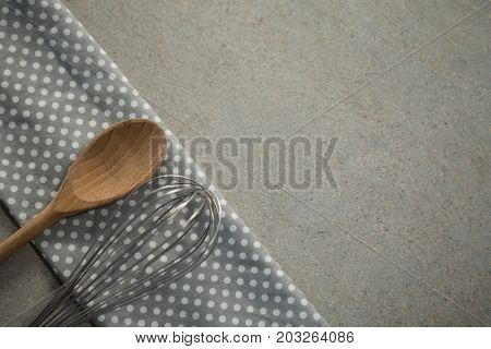 High anlge view of wooden spoon with wire whisk on folded napkin at table