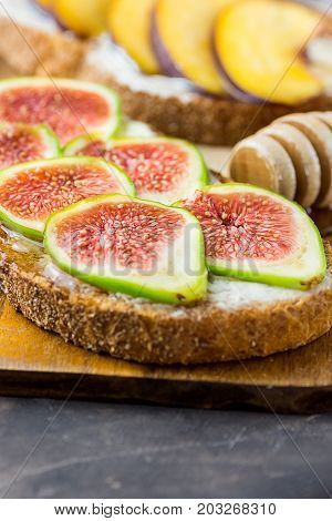 Toasts sandwiches with wholemeal rye bran bread cream cheese or yoghurt ripe figs and peaches. Wood honey dipper on cutting board. Close up.
