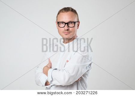 Portrait of a smart serious young man in glasses wearing shirt standing against white background