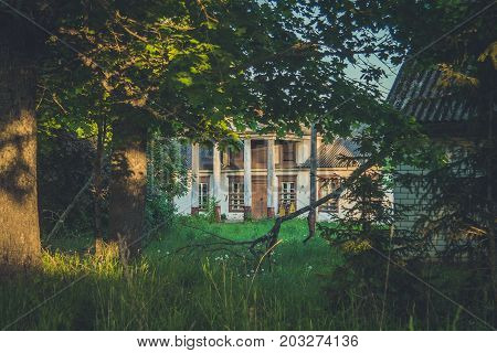 Old Wooden House Among Trees And Tall Weeds