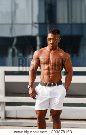 Hot Beautiful black guy with bulging muscles posing against the backdrop of the urban landscape Man fitness model with a beautiful body on the background of the city Shirtless Hunk man without a shirt