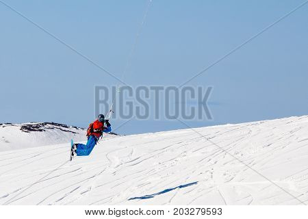 Snowboarder with a kite on fresh snow in the winter in the tundra of Russia against a clear blue sky. Teriberka, Kola Peninsula, Russia. Concept of winter sports snowkite.