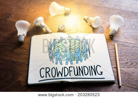 Crowdfunding Concept In Notepad Near Glowing Lightbulbs