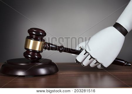 Close-up Of Robot's Hand Hitting Gavel At Wooden Desk