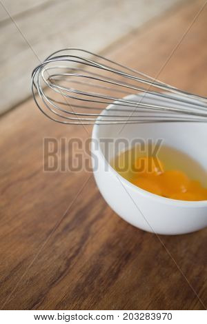High anlge view of egg in bowl with wire whisk on wooden table