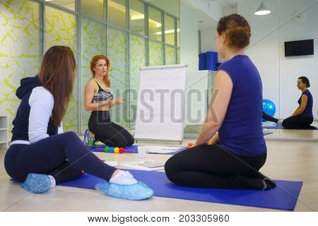 Three women (teacher and two students) are in fitness hall during personal training, focus on teacher