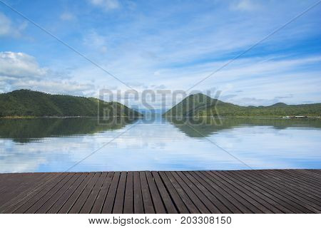 Beautiful sky and mountain with water reflection from Srinakarin, Kanchanaburi, Thailand. Nature background with wooden floor.