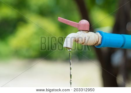 Water drop from old chrome faucet and water pipeline rusty tap with blue pvc pipe. shallow DOF