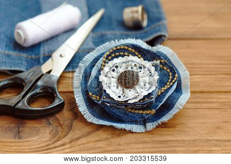 Blue denim flower brooch or hair accessory. Scissors, thread, thimble, needle, old jeans on a wooden table. Recycled denim fabric. Creative uses old jeans. Cheap home craft idea. Closeup