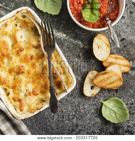 Fragrant homemade casserole with cod and onion in cream sauce with horseradish under a cheese ruddy crust in a form on a gray background with crispy grilled toast. Top View