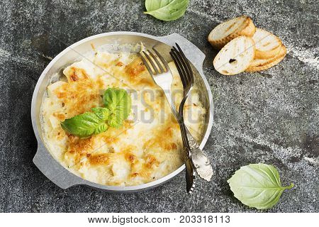 Fragrant homemade casserole with cod and onion in cream sauce with horseradish under a cheese ruddy crust in a form on a gray background with crispy grilled toast. Top View