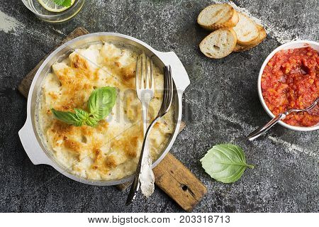 Fragrant homemade casserole with cod and onion in cream sauce with horseradish under a cheese ruddy crust in a form on a gray background with crispy grilled toast. Top View