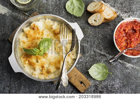 Fragrant homemade casserole with cod and onion in cream sauce with horseradish under a cheese ruddy crust in a form on a gray background with crispy grilled toast. Top View
