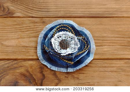 Blue denim floral brooch or hair accessory isolated on a wooden table. How to Recycle old jeans into a new jewelry. Beautiful handmade flower made from recycled materials. Cheap craft idea for adults