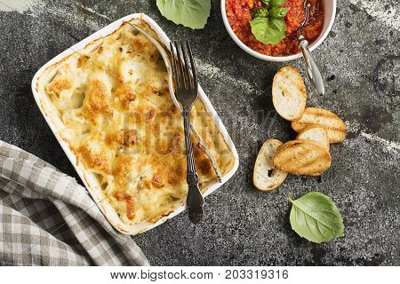 Fragrant homemade casserole with cod and onion in cream sauce with horseradish under a cheese ruddy crust in a form on a gray background with crispy grilled toast. Top View