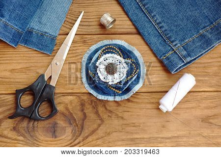 Blue jean flower brooch or hair accessory. Scissors, thread, thimble, needle, old jeans on a wooden table. Denim recycling idea. What to do with torn jeans. Cheap homemade crafts. Closeup