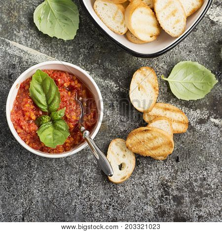 Healthy snack or lunch. Homemade tomato vegetable sauce with garlic, herbs, salt, butter, spices, fresh basil in a ceramic bowl with grilled toasts on a gray stone background. Top View