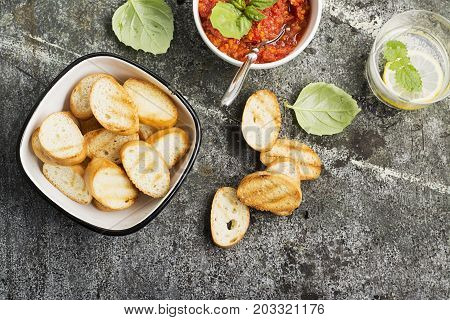 Healthy snack or lunch. Homemade tomato vegetable sauce with garlic, herbs, salt, butter, spices, fresh basil in a ceramic bowl with grilled toasts on a gray stone background. Top View