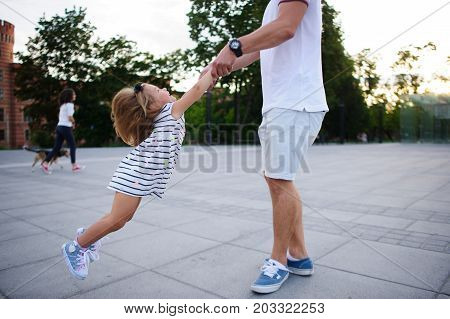 Young dad is playing with a charming little daughter. The man holds the baby by hands and is turned together with her. The child rejoices.