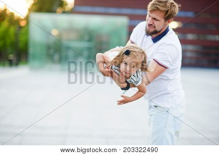 Young dad is playing with a charming little daughter. The man holds the baby on handsand is turned together with her. The child laughs with pleasure.