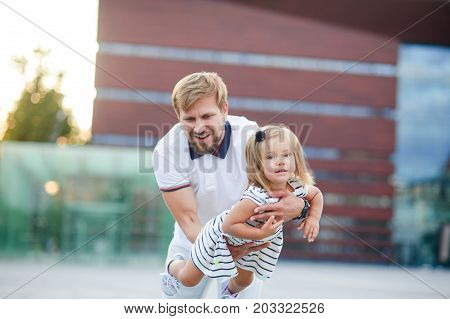 Young dad is playing with a charming little daughter. The man holds the baby on handsand is turned together with her. The child laughs with pleasure.
