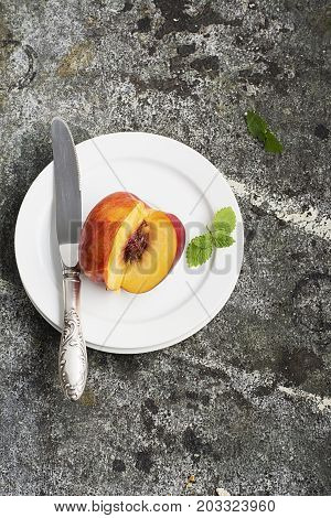 Juicy fresh nectarine on a white plate with a vintage silver knife on a gray stone background. Top View