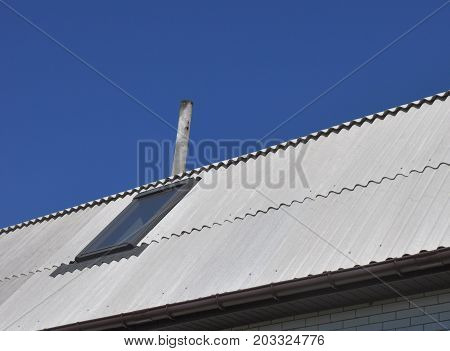 Use of asbestos in buildings is bad for health. Blue sky over the dangerous asbestos new roof tiles with roof window skylights.
