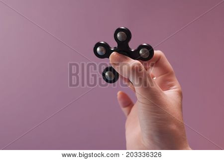 Female hands with a popular toy fidget spinner. Spinning black spinner.Gadget anti stress on a pink background
