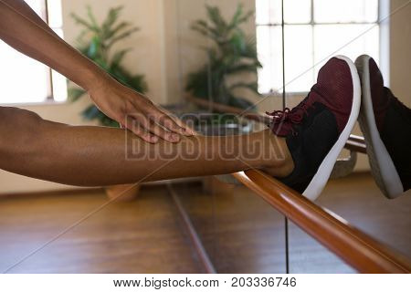 Low section of male dancer stretching leg on barre in sudio