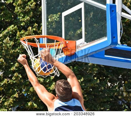 Man is playing basketball outdoors in summer