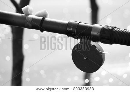 Black-and-white photo with old fishing rod in retro style close-up against the backdrop of lake and bokeh