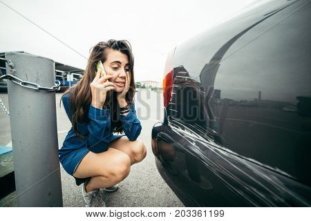 sad woman standing near car with scratch on parking and talking by the phone