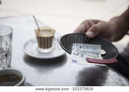 closeup of a young man sitting at a table in the terrace of a cafe paying the bill with a five euros banknote and some coins
