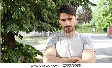 Handsome young man outdoor looking around and at camera with arms crossed on chest