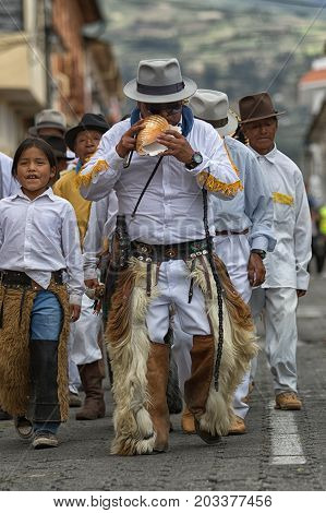 June 29 2017 Cotacachi Ecuador: kichwa indigenous man blowing into a conch shell dancing on the street during Inti Raymi festival