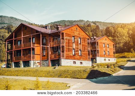 Modern simple and neat wooden duplex-type houses on autumn sunny day with hills of Altai mountains in background yellow lawn and footway on the right; touristic recreation centre in Manzherok Russia