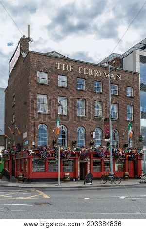 Dublin Ireland - August 7 2017: The historic brick Ferryman pub on the corner of Cardiff Lane and Sir John Rogerson's Quay along Liffey River in the old port. Red framed windows flowers and flags. Street scene.