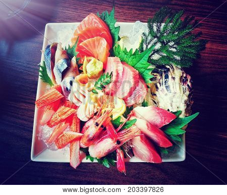 Mixed sashimi set on white plate. Japanese food style with raw fishes, shrimp, surimi (imitation crab meat) keeping fresh on ice decorated with green leaves - cinematic color in film style with flare light