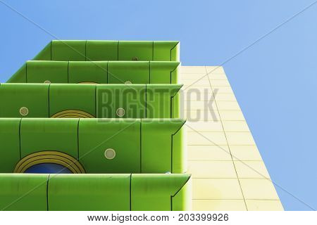 Modern green and yellow building with balconies on blue sky background. Color blocking architecture. Contemporary architecture in green and yellow colors. Colorful modern building. Color blocked hotel