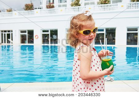 Cute little blonde at the pool and holding achild's cocktail .